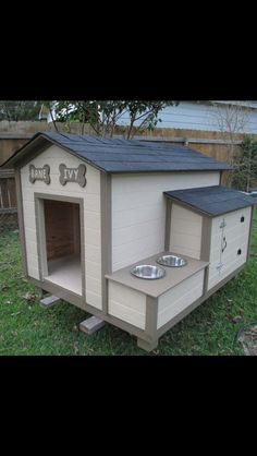 a dog house that is in the grass with its door open and two bowls on it