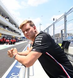 a man leaning on the edge of a race track with his arms crossed and looking at the camera