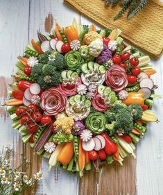 an arrangement of vegetables arranged in a circular arrangement on a wooden surface with flowers and herbs