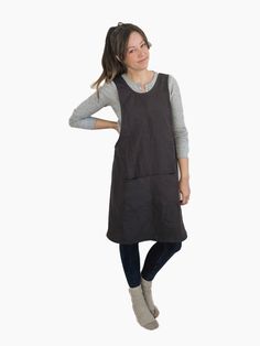 a woman standing in front of a white background wearing a black apron and grey sweater