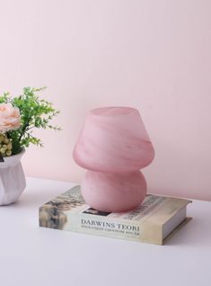 a pink vase sitting on top of a book next to a white vase filled with flowers