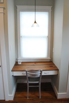 an empty desk with a chair in front of it and a light hanging over the window