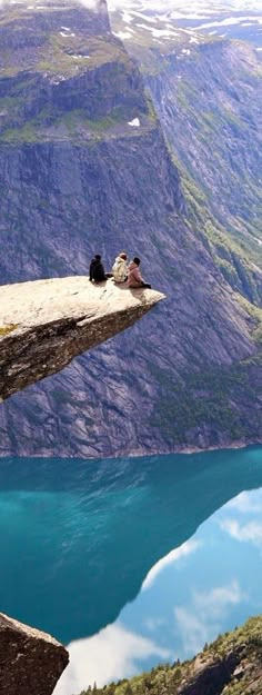 two birds sitting on the edge of a cliff next to a body of water with mountains in the background