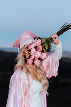 a woman wearing a pink graduation gown and holding a bouquet of roses in her hand