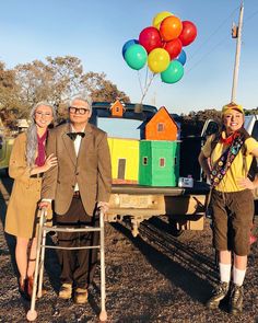 three people standing in front of a house with balloons on top of the back of it