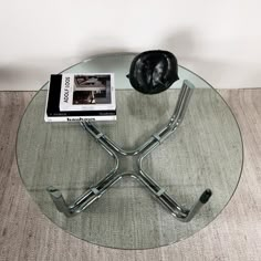 a glass table topped with a metal base and a book on top of it next to a wall