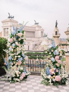 two floral arrangements on the ground in front of an ornate building with statues and columns