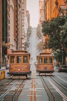 two trolley cars traveling down a street next to tall buildings on either side of the tracks