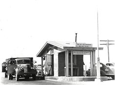 an old gas station with cars parked in front of it and people standing at the pump