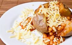 a white plate topped with baked potatoes and beans covered in grated parmesan cheese