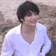 a young man sitting in the sand smiling