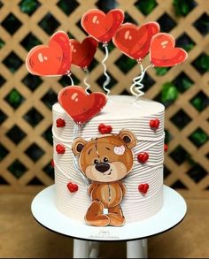 a teddy bear on top of a white cake with red balloons in the shape of hearts