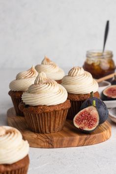 cupcakes with cream frosting and figs on a wooden board next to some fruit