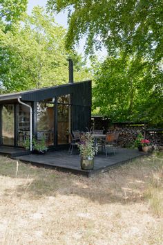 a small black cabin in the middle of a field with trees and grass around it