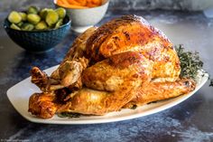 a roasted turkey sits on a plate next to bowls of vegetables