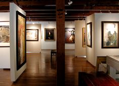 an art gallery with paintings on the walls and wooden floors, along with benches in front of them