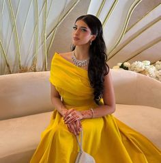 a woman sitting on a couch wearing a yellow dress and holding a white handbag