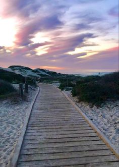 a wooden walkway leading to the beach at sunset with clouds in the sky above it