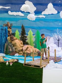 a boy is standing on a bridge in front of a fake mountain and lake scene