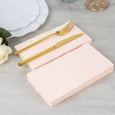 two pink napkins with gold forks are sitting on a white plate next to a rose