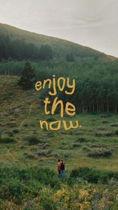 two people standing in a field with the words enjoy the now written on it