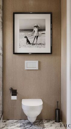 a white toilet sitting next to a bathroom sink under a framed picture on the wall