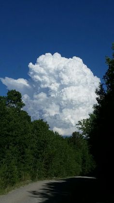 a large cloud is in the sky over a road with trees on both sides and blue skies above