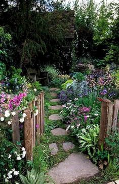 a garden with lots of flowers and plants growing around the stones path leading to an open door