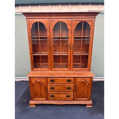 a wooden china cabinet with glass doors and drawers on the top, in front of a wall