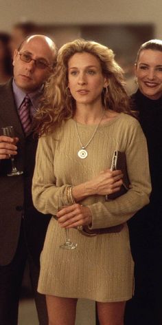 three people standing next to each other with one holding a wine glass in her hand