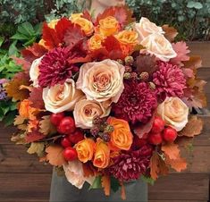 a vase filled with lots of different colored flowers and leaves on top of a wooden table