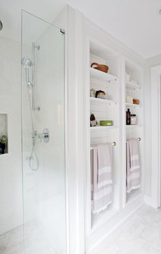 a white bathroom with open shelving on the wall and towels hanging in the shower