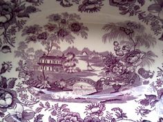 an ornate plate with purple flowers on it and a bridge in the middle, surrounded by greenery