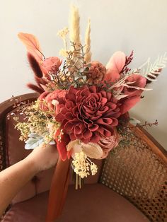 a bridal bouquet is being held up on a chair by someone's hand