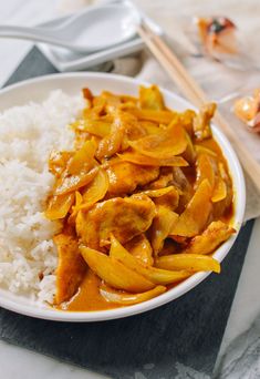 a white plate topped with rice and meat covered in sauce next to chopsticks