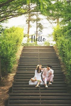 two people sitting on the steps in front of some trees and bushes that say hello