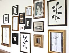 a wall covered in pictures and framed art on white walls next to a brown couch