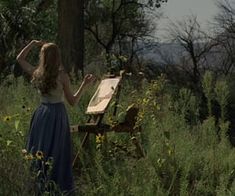 a woman in a long blue dress painting on an easel