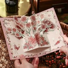 two hands are holding an open card with flowers on it and the inside is pink