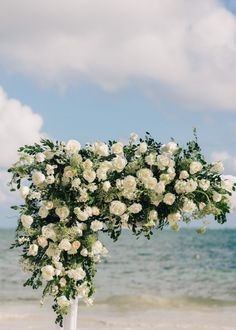 a bouquet of white flowers sitting on top of a wooden table next to the ocean