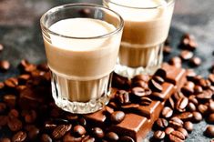 two glasses filled with liquid sitting on top of coffee beans next to some chocolate pieces