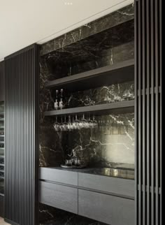 a black and white kitchen with marble counter tops, cabinets and wine glasses on the shelves