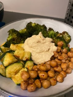 a white plate topped with potatoes, broccoli and chickpeas next to a bowl of mashed potatoes