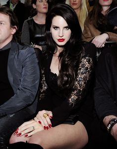 a woman with long black hair and red nails sitting in front of a group of people