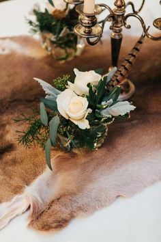 a table topped with candles and flowers on top of a fur covered table cloth next to a candelabra