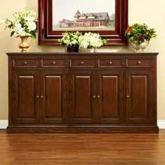 a wooden sideboard with flowers on it in front of a framed painting and wood flooring