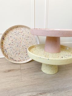 two cake plates sitting next to each other on top of a wooden floor covered in sprinkles