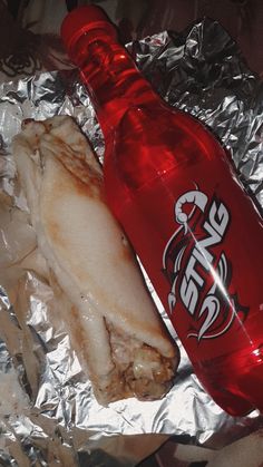 a soda bottle sitting next to a sandwich on top of tin foil covered in aluminum foil