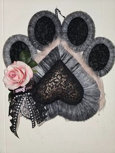 an animal paw made out of yarn and lace next to a pink rose on a white wall