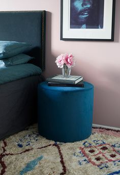 a bedroom with pink walls and a blue ottoman next to a bed, framed photograph on the wall